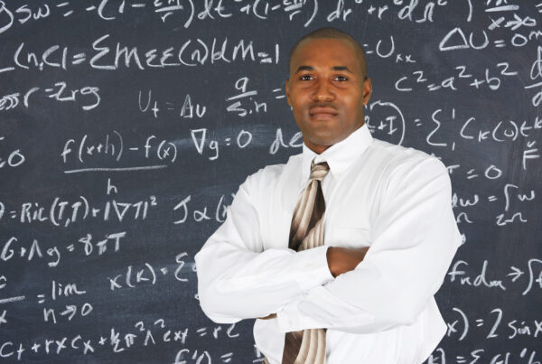 A black man standing in front of a blackboard with formulas on it.