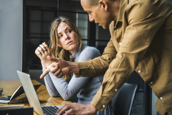 A man and woman sitting at a desk with a laptop in front of them.